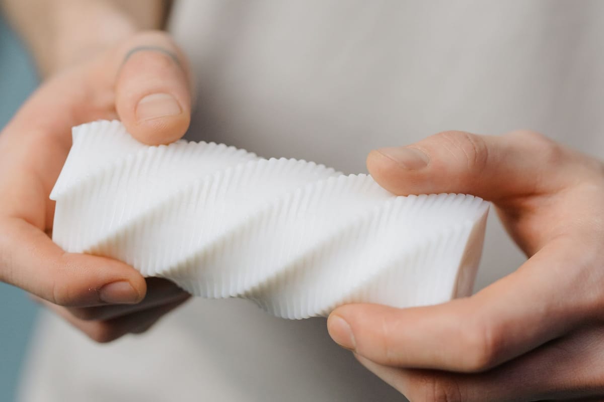 Manos sosteniendo con cuidado una pieza espiral impresa en 3D en blanco.