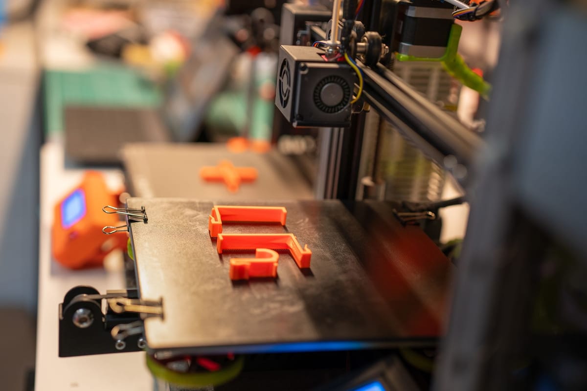 Piezas pequeñas impresas en 3D en naranja sobre la cama de impresión del taller.