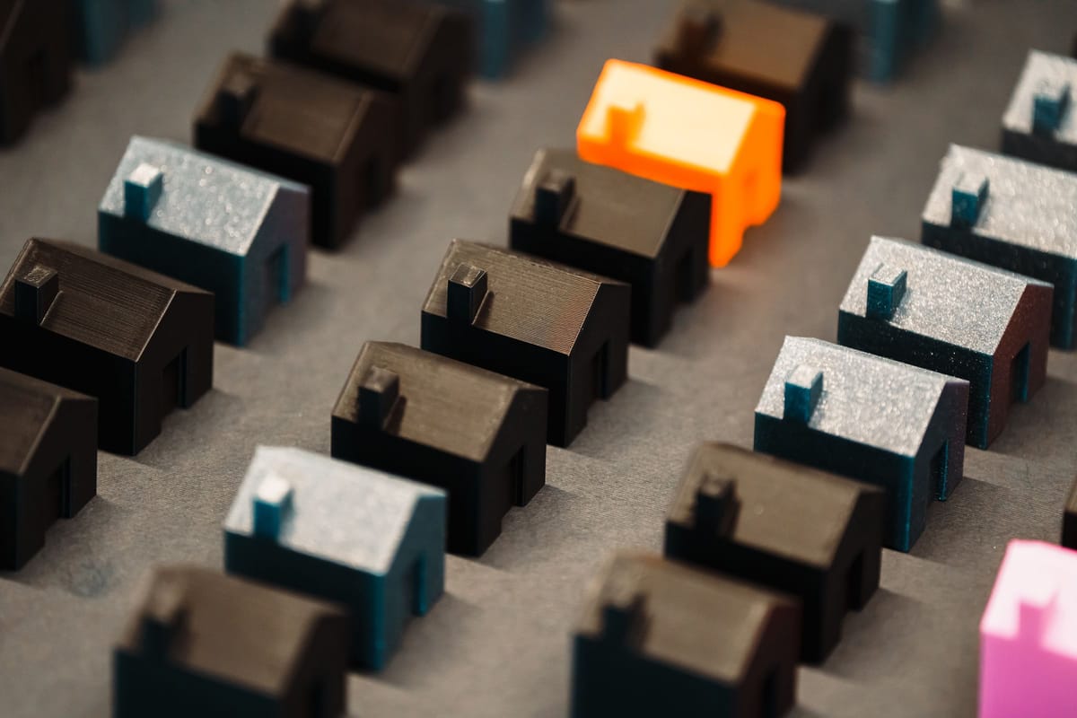 Filas de casitas impresas en 3D, todas iguales, con una pieza naranja que resalta entre la serie.